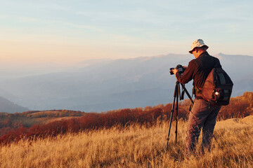 Male photographer standing and working at majestic landscape of autumn trees and mountains by the horizon