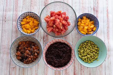 ingredients for a poke in a bowl. Tomatoes, black rice, tuna or salmon, mango and soybeans