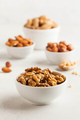 A handful of walnuts in a white bowl, assorted nuts on a light background. Healthy snacks, healthy...