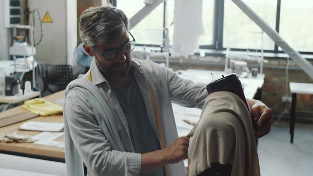 Mid-aged male fashion designer putting fabric on mannequin and pinning it while working in tailoring studio