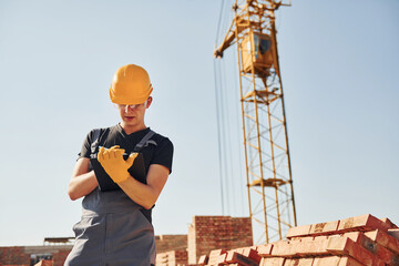 Holds notepad with documents. Construction worker in uniform and safety equipment have job on building