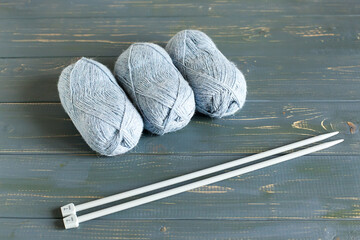 gray balls of yarn and plastic knitting needles on a wooden table. Needlework concept