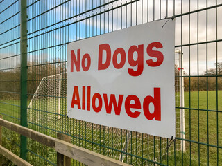 Large "No dogs allowed" sign on the fence of a village football field village of St Dogmaels.