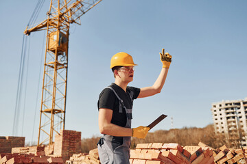 Shows gestures and talks. Construction worker in uniform and safety equipment have job on building