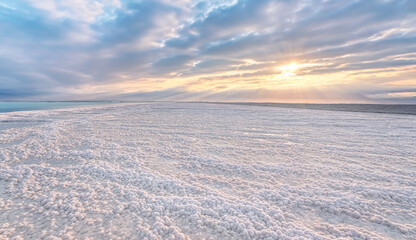 Crystalline white salt beach lit by morning sun, small puddles with seawater at Dead Sea - world most hypersaline lake