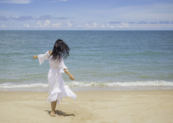 Fototapeta na wymiar Blurred motion of young woman wearing white dress feeling happy,having fun,relaxation on the beach with windy and sunshine during vacation.