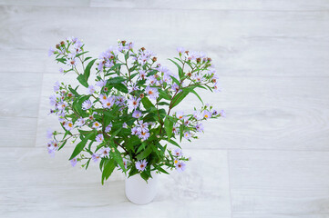 Wild purple flowers in a white vase on  wooden floor.