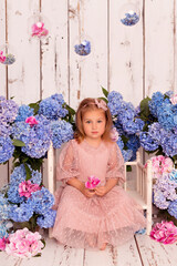 Fototapeta premium Happy baby girl in a dress in the studio on a white background with pink and blue hydrangea flowers