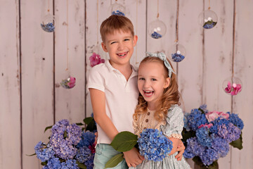 Happy baby boy and girl in studio on white background with pink and blue hydrangea flowers