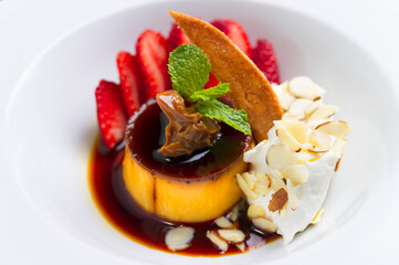 creamy pudding with caramel sauce, sliced  strawberry, whipped cream, almond slices, cookie, mint in white plate