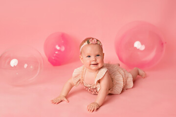 Happy baby girl on a pink background with balloons. Celebration. Birthday