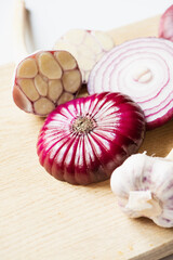 close up view of red onion and garlic on wooden cutting board on white background