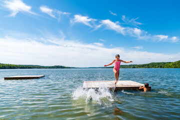 Young girl in pink bathing suit jumping off of raft into lake 
