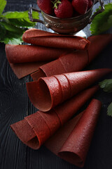 The natural sweetness of strawberries rolled in a tube. Natural product. Vertical photo on a black background. Flat layout.
