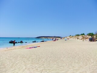 Fototapeta na wymiar Pink beach in Crete. Sandy coast, azure sea. Tourists swim in the sea and sunbathe.