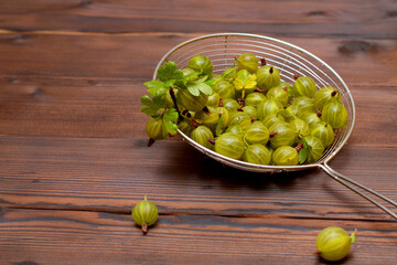 green gooseberries in a steel strainer on a wooden table in the kitchen