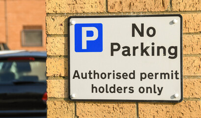 Sign on a building notifying drivers of a restricted parking area.  A parked car is in the background. No people.