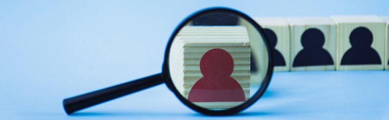 selective focus of magnifying glass near wooden block with red human icon on blue background,...