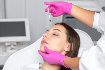 Cosmetologist makes rejuvenating anti wrinkle injections on the chin, cheeks and neck of a...