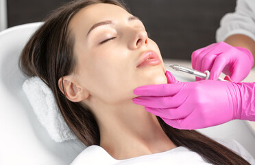 Woman with beautiful clean skin. Cosmetologist does injections for lips augmentation and anti...