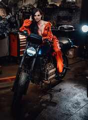 Sexy looking brunette in work overalls sitting on a black motorcycle in a car service
