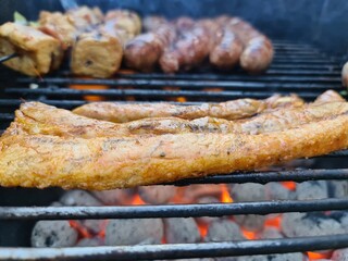 Bauchfleisch sowie Bratwurst und Fleischspieße auf einem Grill