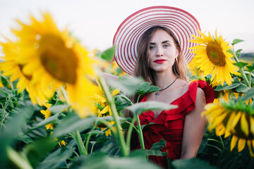 A young, slender girl in a red dress poses in a field of sunflowers