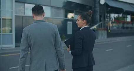 Two managers, a man and a woman, walk on the street against the background of a modern building and discuss a business plan while walking around the city. Work plans for the week