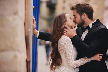 Wedding couple kissing in the old city. Blue vintage doors and cafe in ancient town on background....