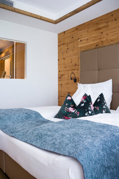 Cozy hotel bedroom interior in alpine chalet style. Modern double bed with blue blanket and pillows against rustic wooden wall decoration, comfort room design