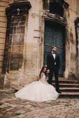 Stylish bride and groom gently hugging on european city street. Gorgeous wedding couple of newlyweds embracing near ancient building. romantic sensual moment of newlyweds