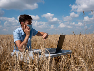 Naklejka na ściany i meble business men at remote work. A young man wearing a Covid-19 mask works for a laptop in a wheat field.