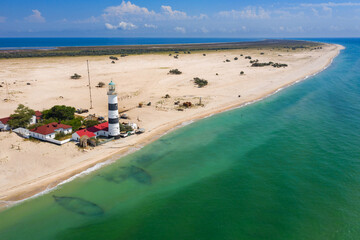 aerial view to buildings and lighthouse on the beach with emerald water under blue sky and copy space