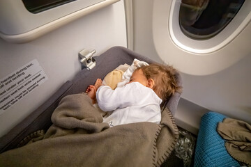 Small two year old baby girl sleep in a bassinet on a airplane