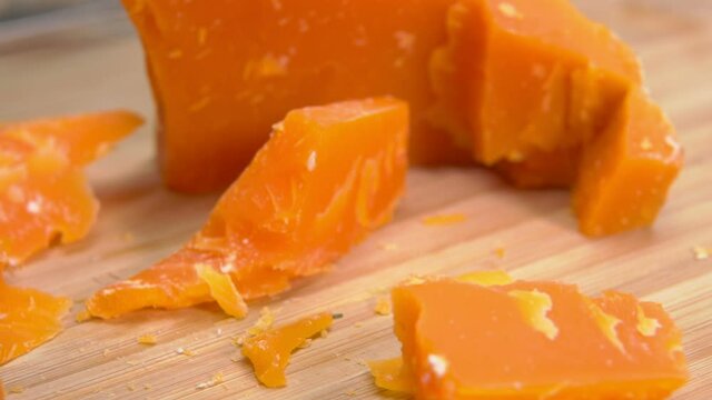 Knife cuts and breaks a delicious hard french orange-colored Mimolette cheese on a wooden board