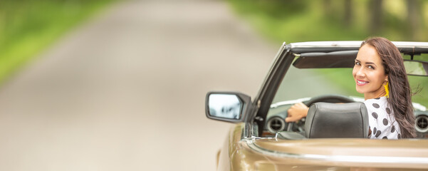 Woman driving in a cabriolet looks back and smiles into the camera.