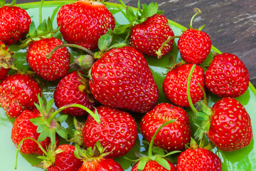 Fresh ripe juicy strawberries on the orange plate on a wooden background