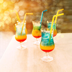 Glasses of rainbow cocktails with straws on the table at sunset. Summer holidays. 