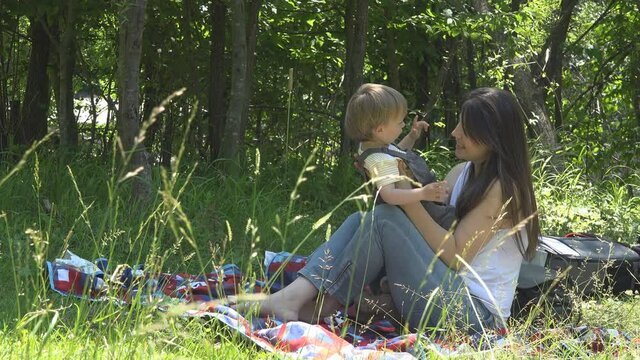 Mother sitting on green grass and lifting up baby, happy joy