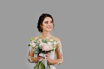 Bride with wedding bouquet smiles, looks right side and touches her face. Attractive girl for social networks. Girl in wedding gown on blank background