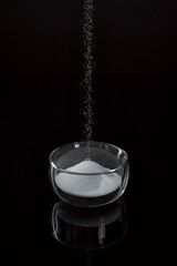 Obraz na płótnie Canvas Salz und Zucker fallen in eine Glas Schüssel auf schwarzer reflektierender Oberfläche
