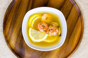 Top view of white bowl with traditional light spicy thai cuisine tom yam soup with shrimps, seafood and lemon on wooden board background.