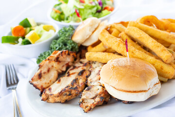A view of a chicken dinner, featuring slider buns, deep fried zucchini fries, and french fries, in a restaurant or kitchen setting.