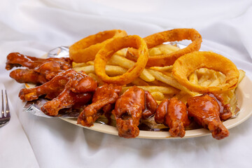A view of an appetizer plate with buffalo wings, onion rings and french fries, in a restaurant or kitchen setting.