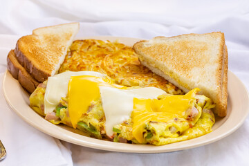 A view of a vegetable omelet plate, featuring white bread toast and shredded hash browns, in a restaurant or kitchen setting.