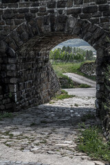 Fototapeta na wymiar Old Stone Portal With Cobblestone Road To Rural Landscape