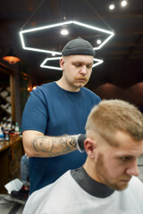 Vertical shot of a professional barber serving young handsome man sitting in barbershop chair. Focus on barber
