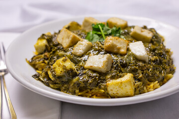 A view of a plate of palak paneer, in a restaurant or kitchen setting.