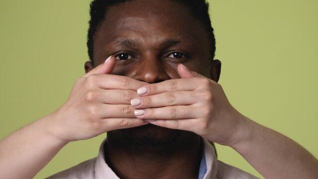 Female hands covering mouth of African-American man on color background. Stop racism