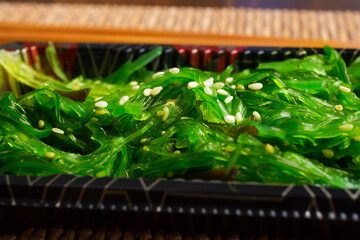 A closeup view of a container of wakame salad, in a restaurant or kitchen setting.